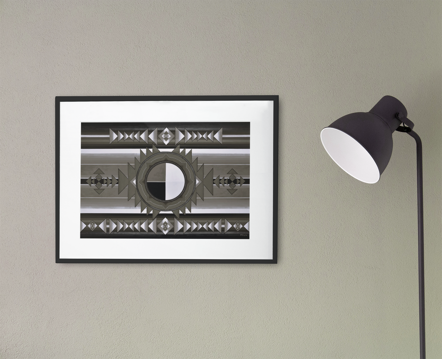 A small black and white Indigenous Medicine Wheel giclee art print, framed in black with white matting, hanging on the wall next to a black lamp
