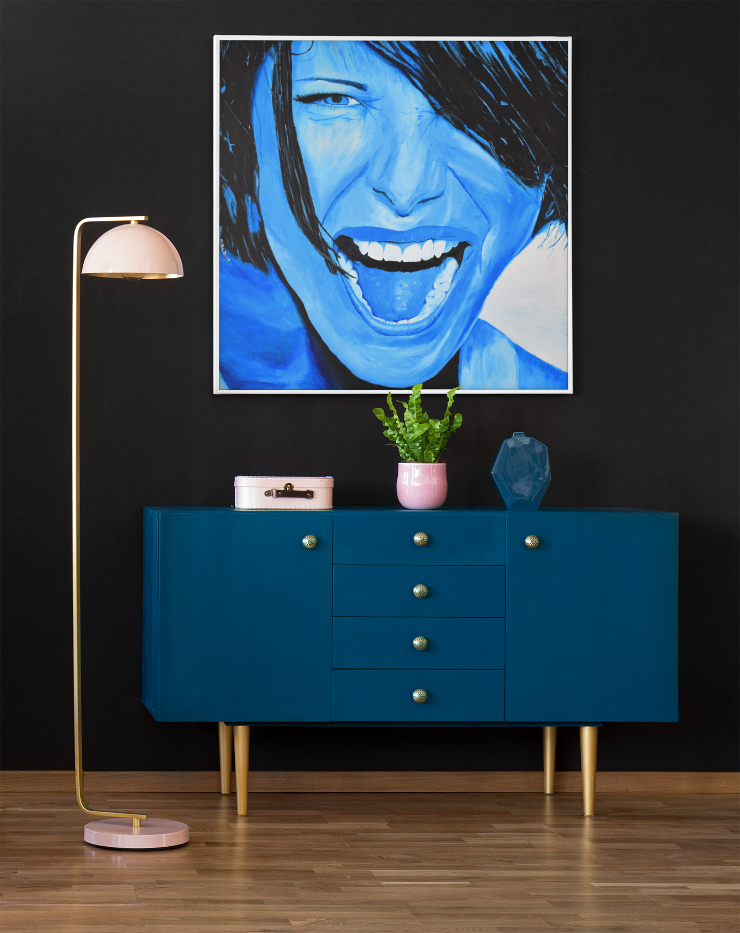 An art print on canvas of a passionate woman showing emotions, painted in bright blue, hanging on a wall over a cabinet next to a lamp, woman portrait art