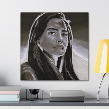 A black and white Indigenous art print on canvas of an Aboriginal Woman with a feather earring, hanging on the wall over a desk next to a lamp