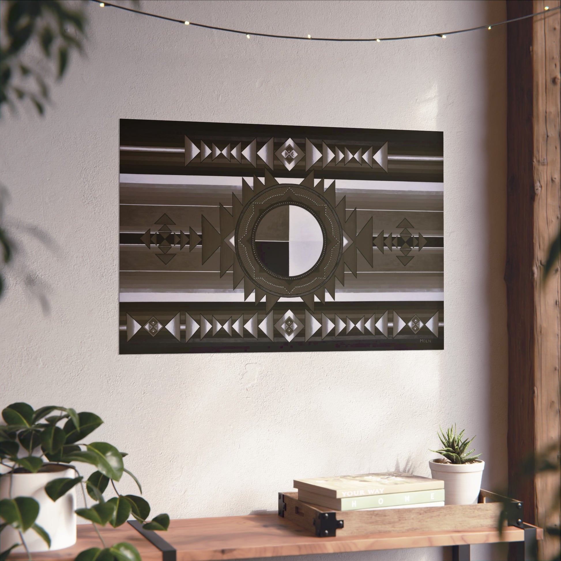 A black and white Indigenous Medicine Wheel giclee art print hanging on the wall over a wooden table next to a plant