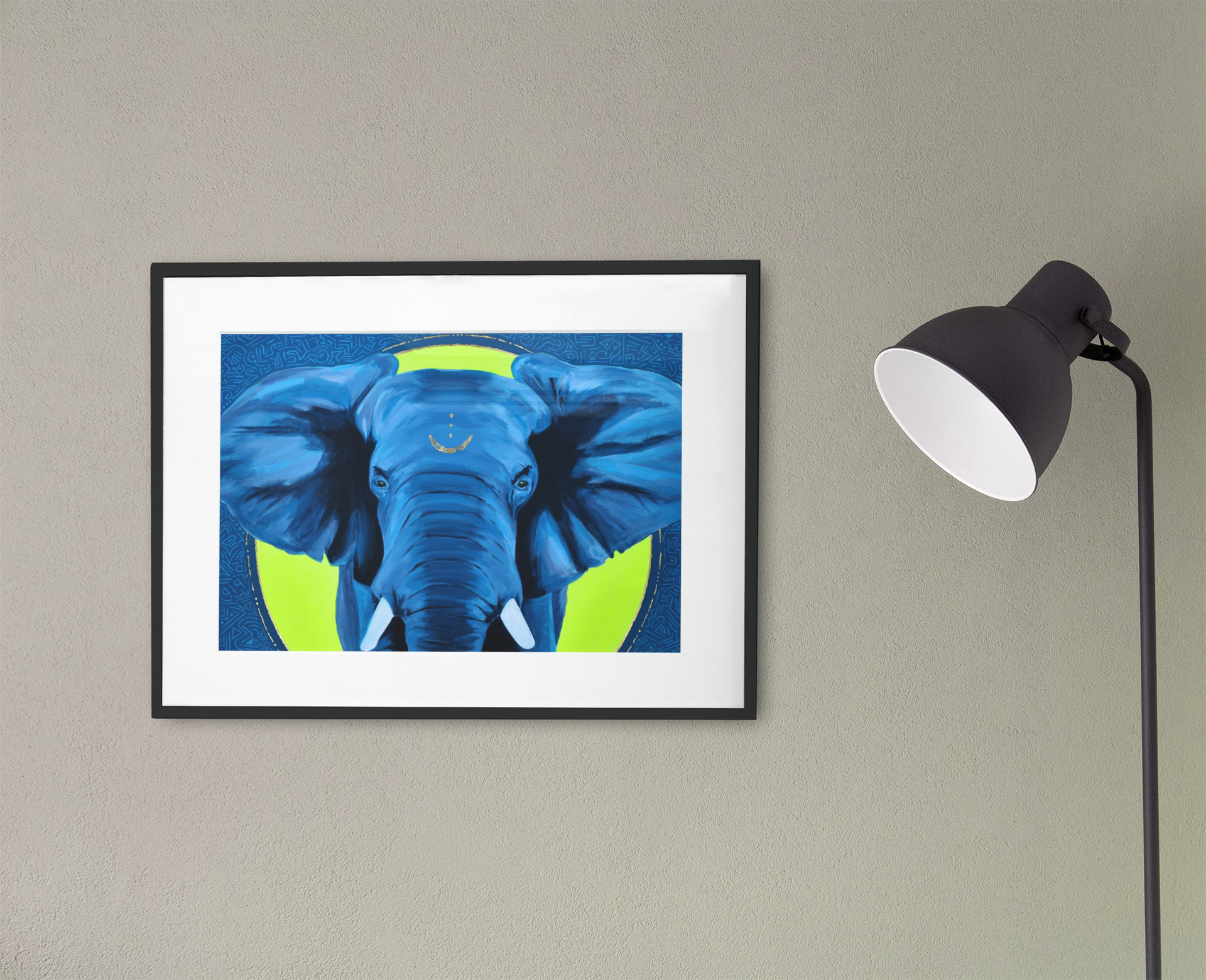 A blue and yellow African Elephant art print in a black frame with white matting hanging on a wall next to a lamp