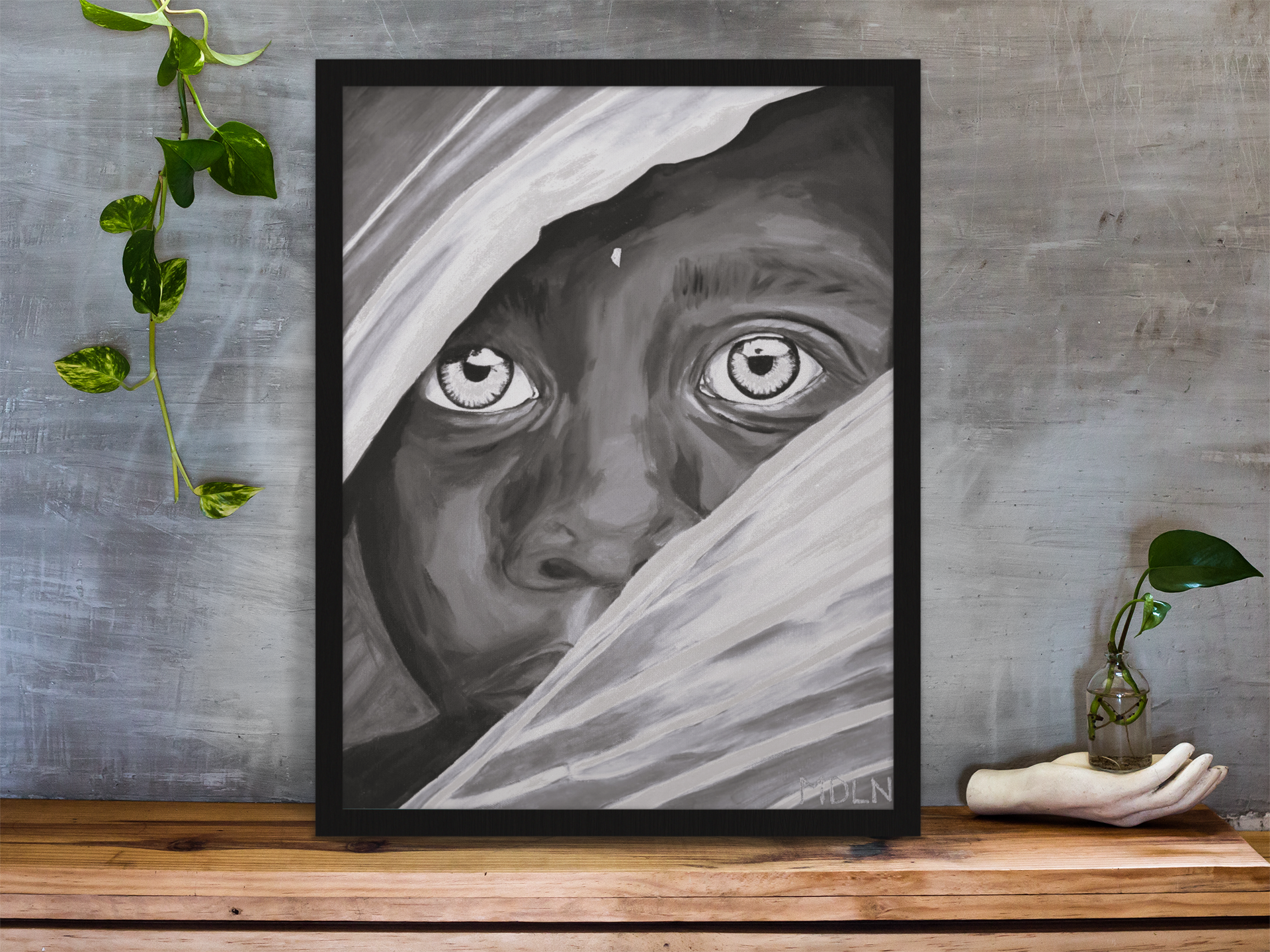 A black and white art print on canvas, framed, of an African boy, leaning up against a wall sitting on a desk