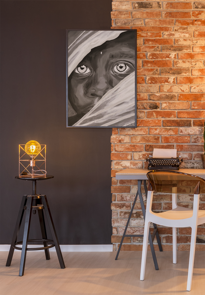 A large black and white art print of an African Boy hanging on a brick wall over a desk and lamp
