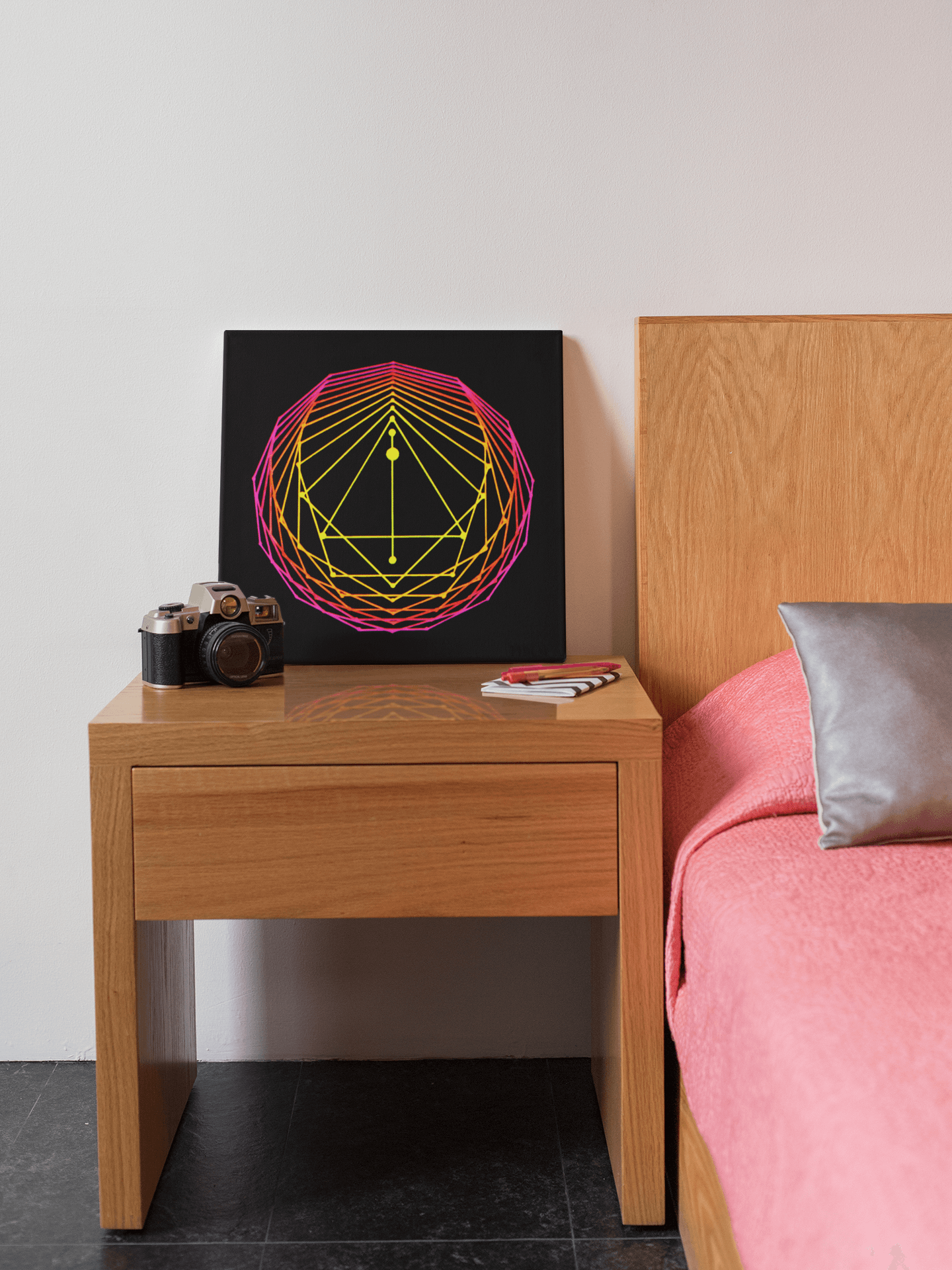 Canvas print of an original acrylic painting of sacred geometry art in pink/orange/yellow tones, leaning against a wall on a bed side table