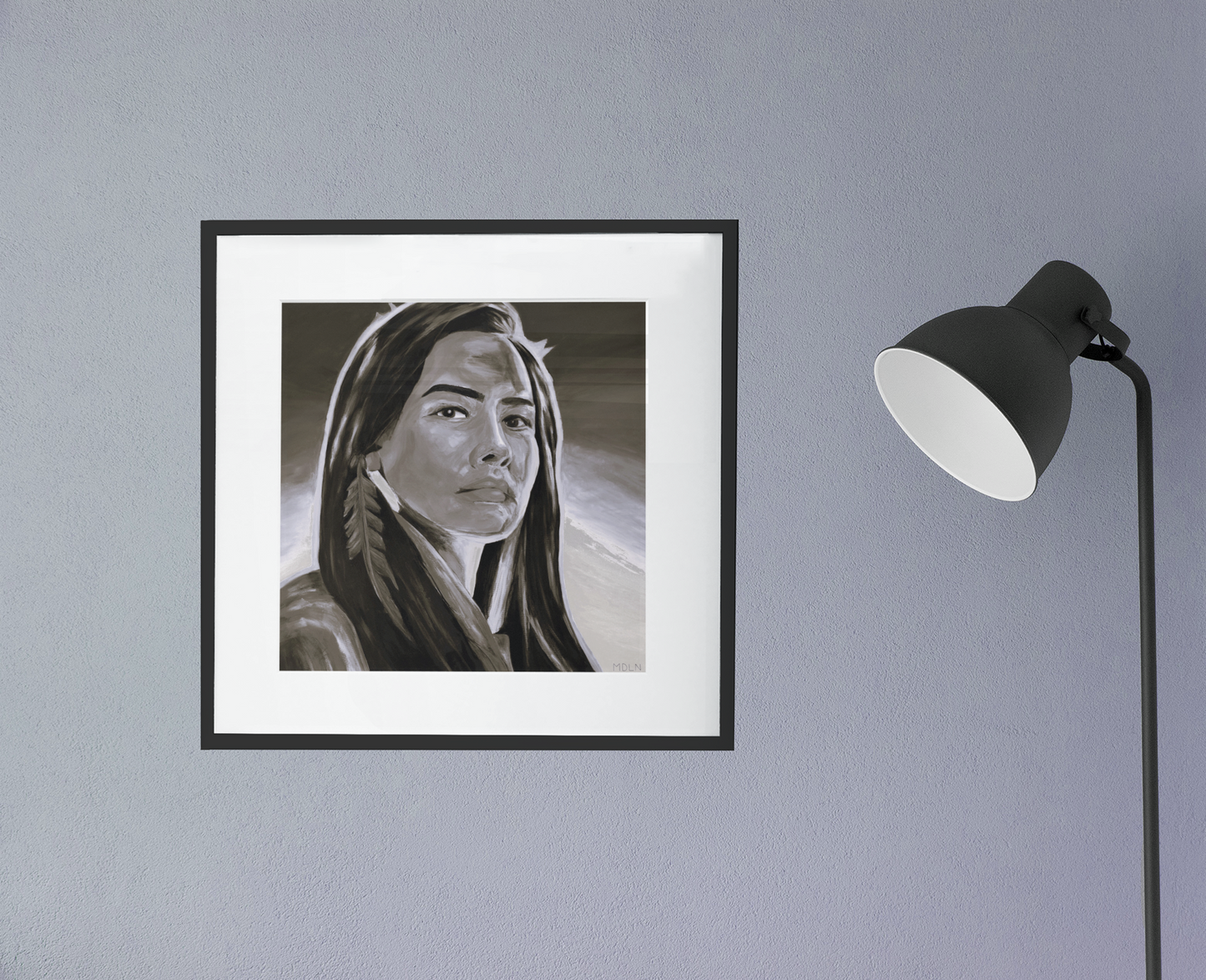 Stunning black and white Indigenous giclee art print of an Aboriginal Woman, framed in black with white matting, hanging on a wall next to a lamp