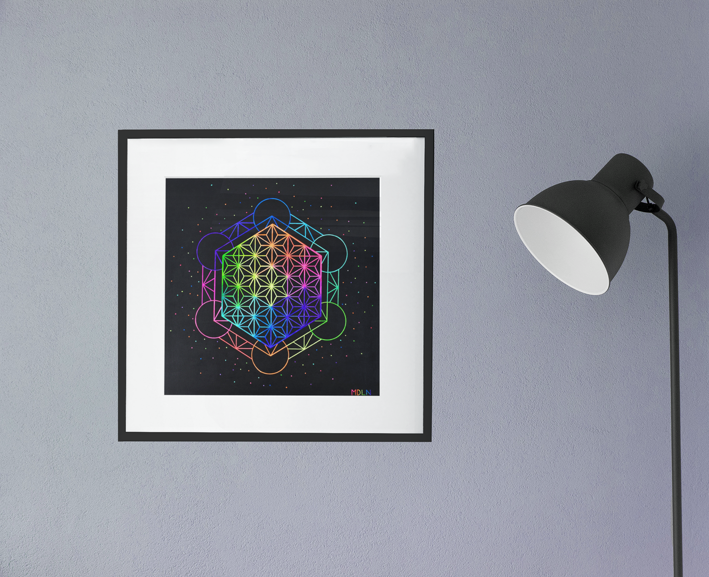 A bright and colorful sacred geometry giclee art of Metatrons Cube sacred geometry art overlayed by the flower of life sacred geometry art, framed in black with white matting, hanging on a wall next to a lamp