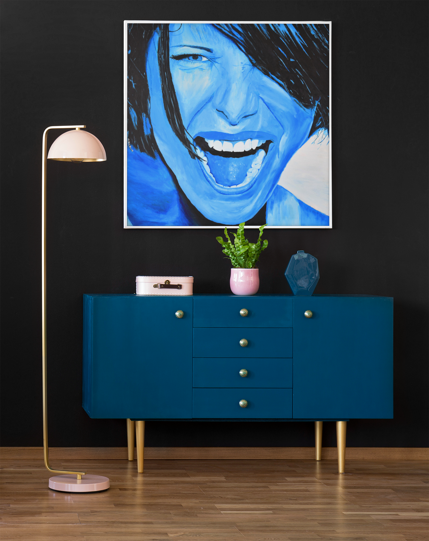 A bright blue giclee art print of a passionate woman showing emotions, woman portrait art, hanging on a wall over a cabinet next to a lamp
